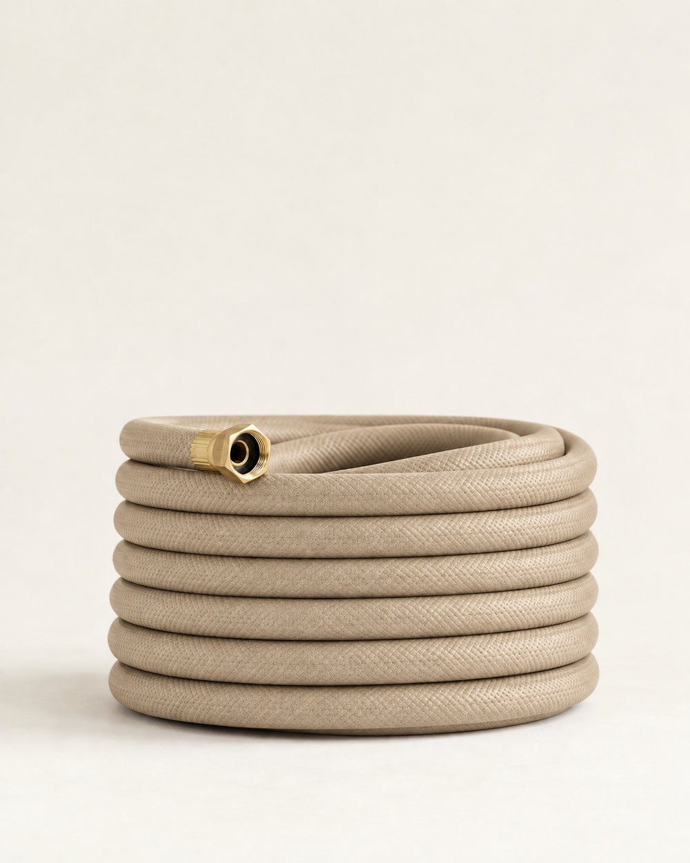 Sand beige garden hose with brass fittings coiled on a cream studio background