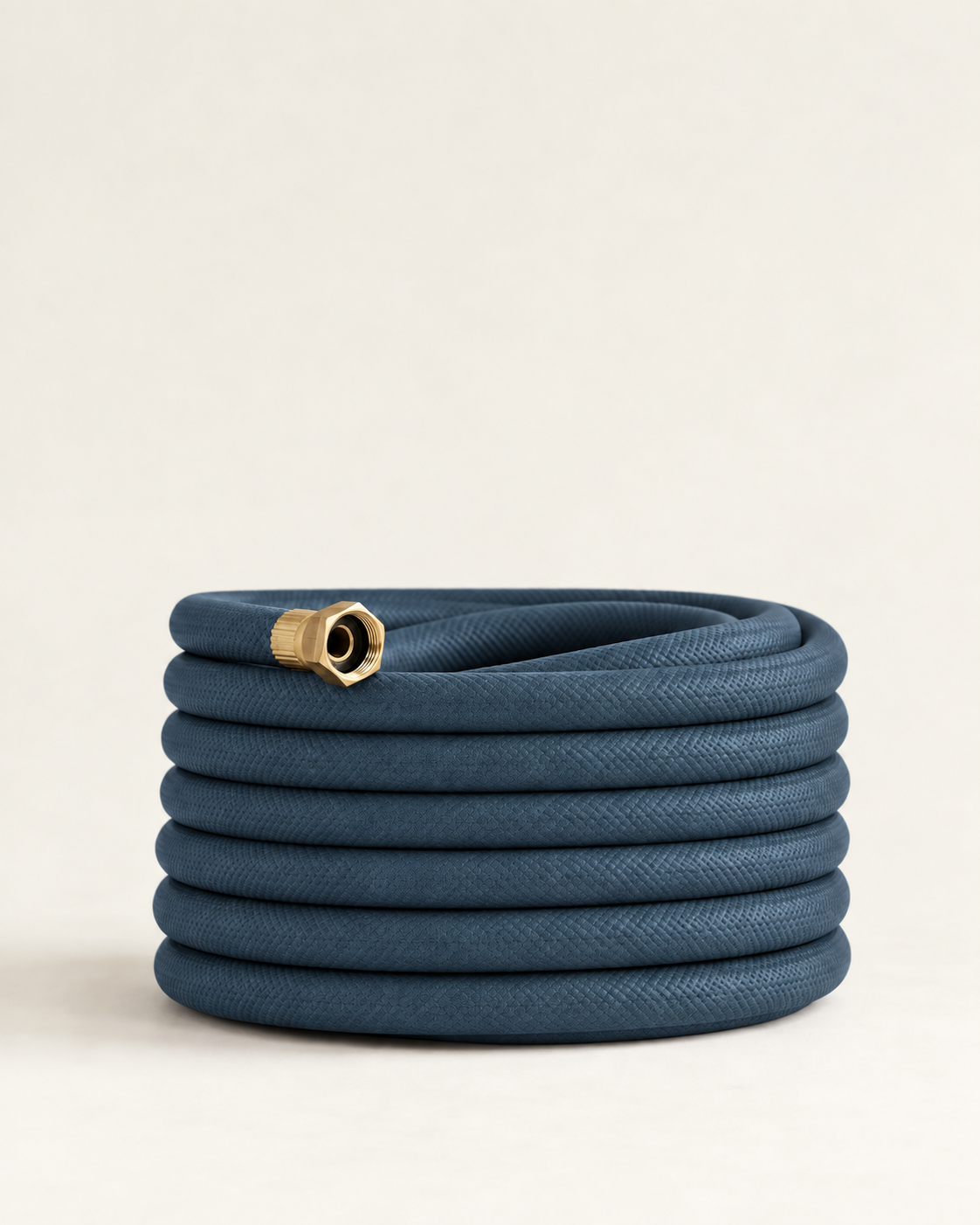 Slate blue garden hose with brass fittings coiled on a cream studio background
