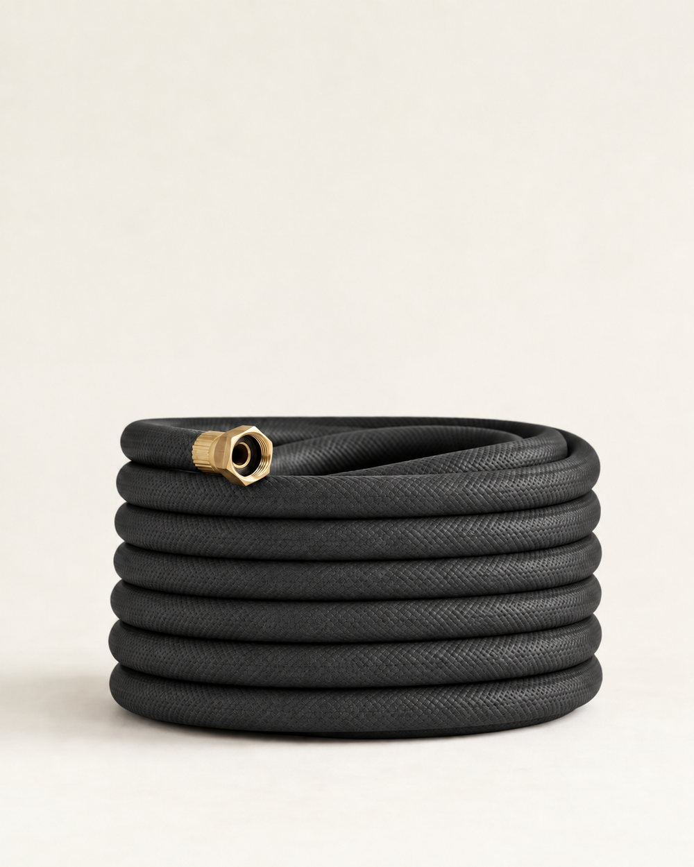 Charcoal black garden hose with brass fittings coiled on a cream studio background