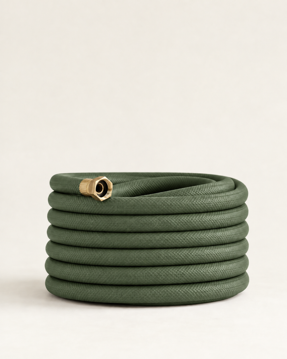 Olive green garden hose with brass fittings coiled on a cream studio background