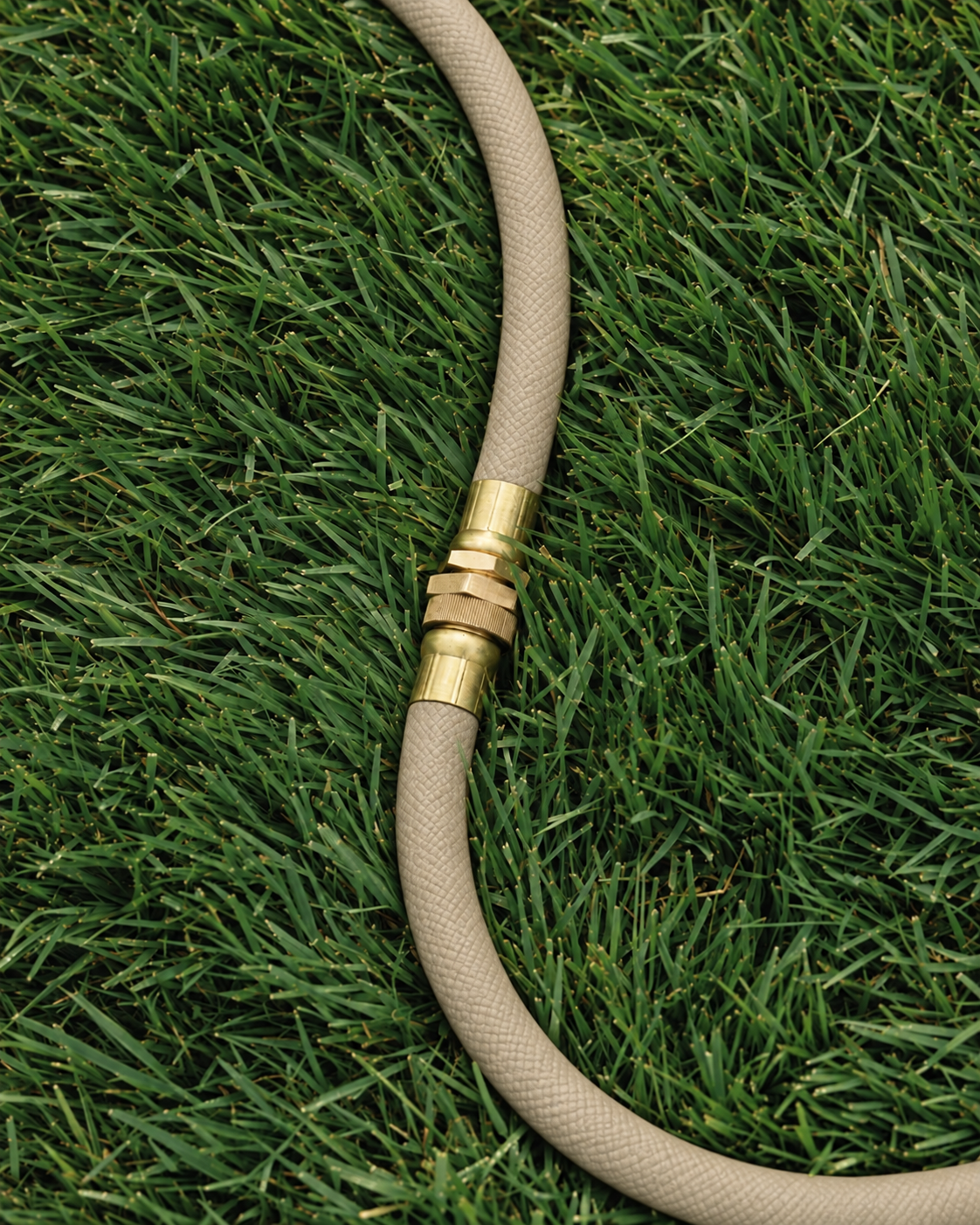 Brass garden hose connector on a sand beige woven hose over grass