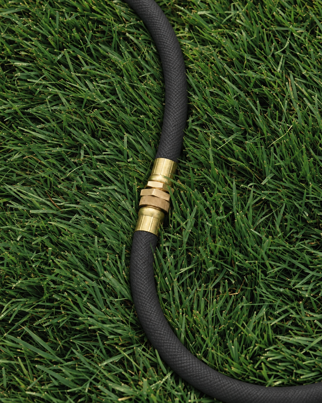 Brass garden hose connector on a charcoal black woven hose over grass