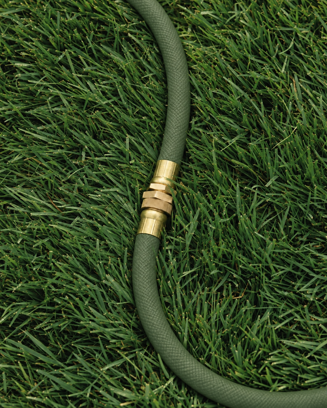 Brass garden hose connector on an olive green woven hose over grass